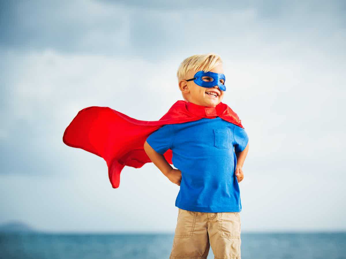 Smiling boy with superman style red cape and mask